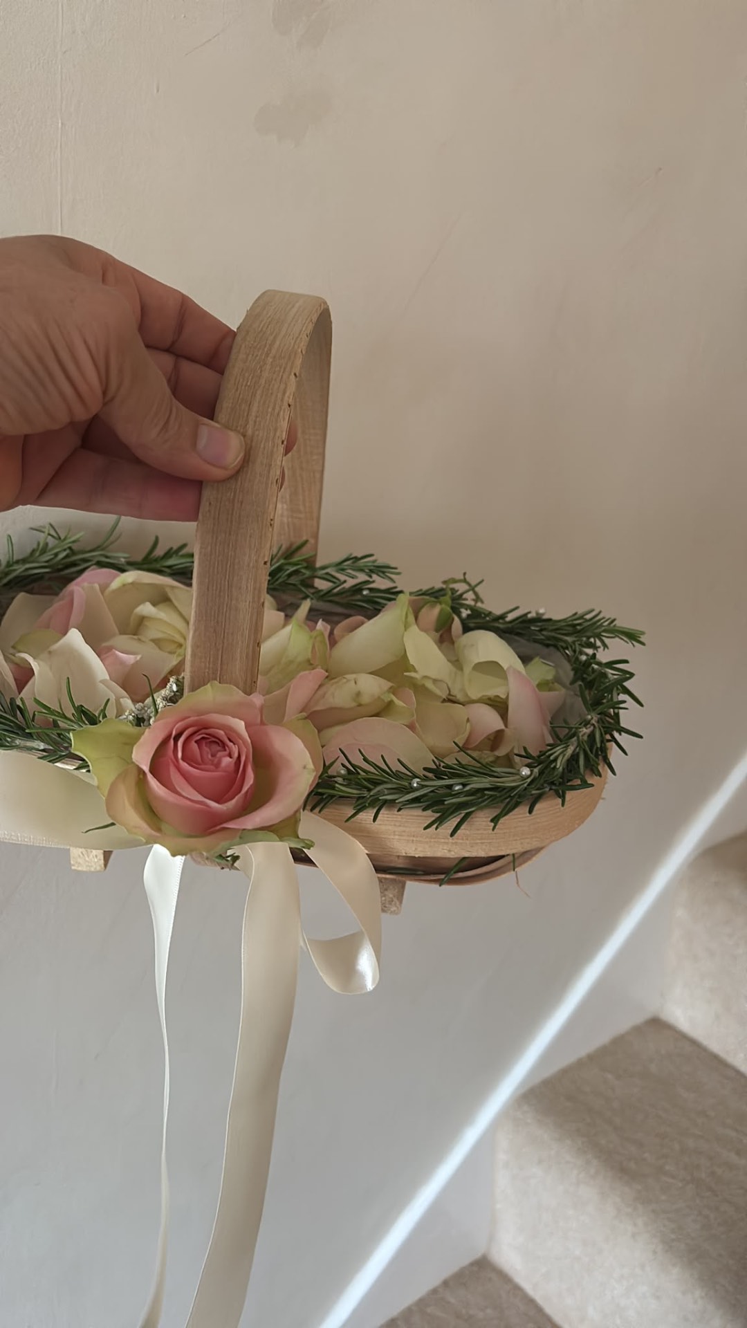 Wooden flower girl basket lined with rosemary, blush rose petals, and a pink rose with cream ribbon