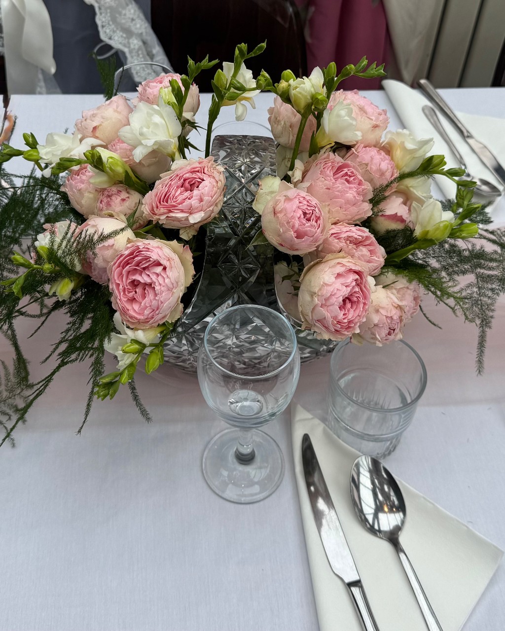 Pink garden roses and white freesias arranged in a cut-crystal vase on a wedding table