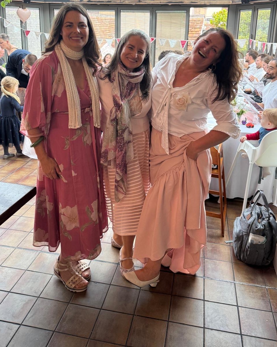 The three Flower-girls laughing together at a celebration in a glass-roofed conservatory