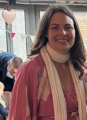The angel cake maker smiling in a pink floral dress and cream knitted scarf