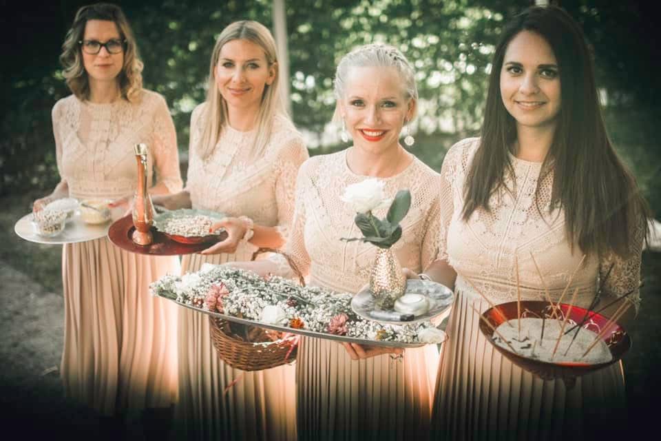 Four attendants in blush dresses carrying floral and ceremonial details